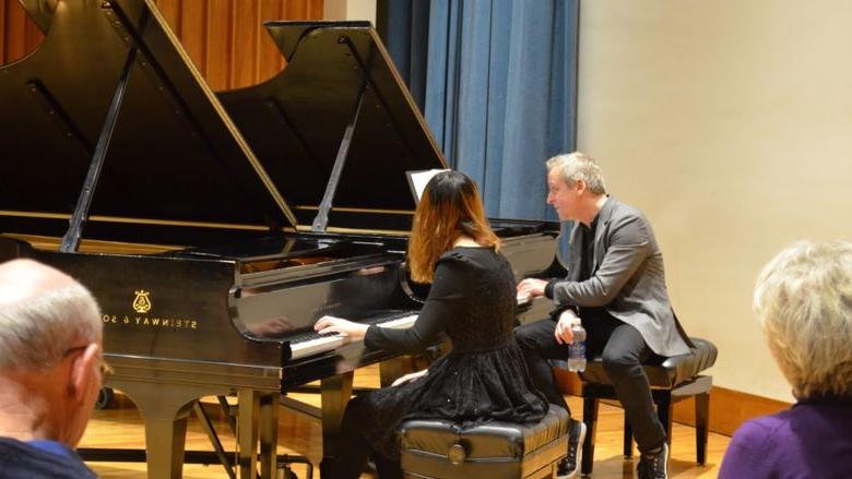 一个男人和一个女人分别坐在自己的钢琴前，而他在指导学生音乐家.